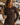 A woman wearing a dark brown long-sleeve rash guard and matching swim shorts stands on a sunny poolside deck holding a drink. The rash guard has 'BON SOUL' printed on the chest in white and pink.