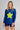 Woman wearing a blue long-sleeve shirt with a yellow star and dark shorts on a gray background