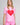 A woman modeling a light pink short-sleeve t-shirt with a large red heart graphic on the front, paired with matching pink shorts, against a light gray studio background.