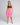 A woman modeling bright pink drawstring shorts and a dark brown sports bra against a light gray studio background.