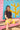 Woman sitting on a beach hut step wearing a brown short sleeve rashguard and long yellow swim shorts.