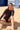 Woman sitting on a sandy beach wearing a brown long sleeve rashguard and brown bather shorts. 