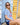 Woman wearing navy bather shorts and striped rashguard sitting in front of a beach hut