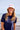 Woman wearing a white cap featuring the words LE VIBE in red, and a navy blue short sleeve rashguard, standing on a beach.