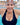 A woman in a black swimsuit and mirrored swim goggles takes a selfie at an indoor swimming pool.