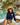Woman sitting by a pool with palm trees and a hut in the background, wearing a long sleeve navy rashguard featuring a white heart design with the word AMOUR on the left side of her chest