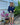 A woman stands in a backyard garden setting wearing a navy blue long-sleeve top, leopard print shorts, a white cap, and white sneakers with red laces.